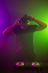 DJ at work mixing sound on her decks at a party or night club with colourful smoke light background