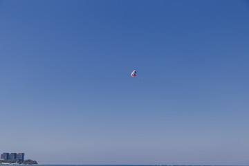 Spectacular scenic view on the sea and blue sky with people flying on a colorful parachute towed by a motor boat.