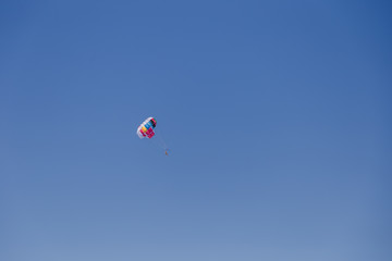 Spectacular scenic view on the sea and blue sky with people flying on a colorful parachute towed by a motor boat.