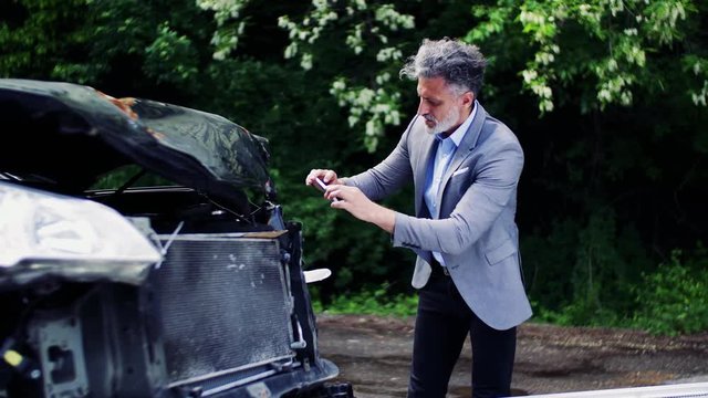 Mature man taking pictures of a broken car after an accident.