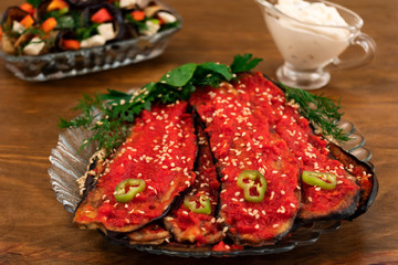 Vegetable appetizer of eggplant with spicy adjika, decorated with sprinkles of sesame seeds, pieces of bitter pepper and fresh basil, dill and parsley.