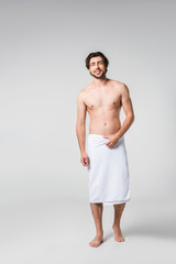 smiling handsome man in white towel on grey backdrop