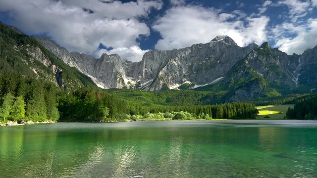 Alpine lake Fusine, Italy. Landscape with clear lake, green trees, meadow and mountains. Panning shot. 4K