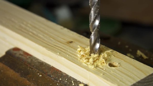 Drilling machine drilling through a fine peice of furniture wood, with bits of wood and saw dust