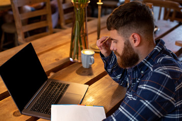 Young man chatting via net-book during work break in coffee shop, male sitting in front open laptop...