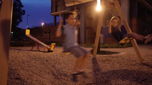 Two boys at playground enjoying at night in open air. Boys are playing otdoors at night