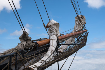 bowsprit and jib boom with reefed sails on the bow of a historic sailing ship against a blue sky...