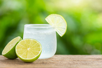 Glass of iced lemon soda on wooden table with green blur space for text or design