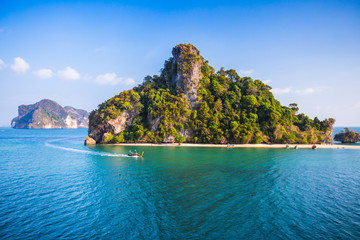 Obraz premium Traditional longtail Thai boat moves in a calm sea near the tropical green island with a beach. Thailand