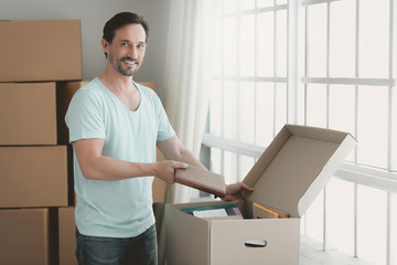 Obraz na płótnie Canvas Happy Young Guy Unpacks Cardboard Box in Room.