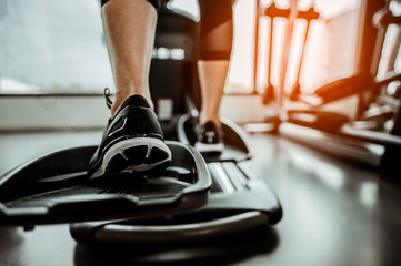 Closeup leg of cardio workout on an elliptical.people working out on an elliptical trainer in gym.Back view - obrazy, fototapety, plakaty
