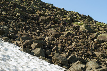 fragment of a stone scree on a slope on the edge of a melting glacier and a blue summer sky
