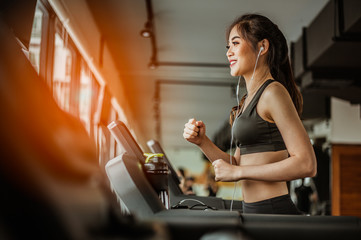 Fototapeta na wymiar Portrait of Fitness woman running on treadmill in gym listening to music.exercising concept.fitness and healthy lifestyle.