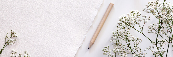 Panoramic copy space of handmade paper with white field flowers and a wooden pencil