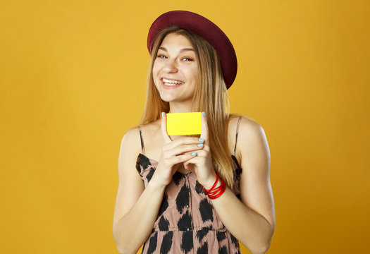 Young happy beautiful woman holding empty credit card in hands over orange background