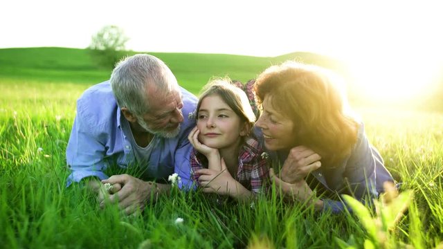 Senior couple with granddaughter outside in spring nature, relaxing on the grass.