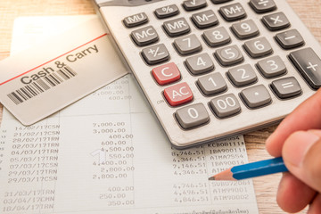 Fototapeta premium The fingers are holding the pencil. Below is a calculator, a bank book, a cash card placed on a wooden desk.