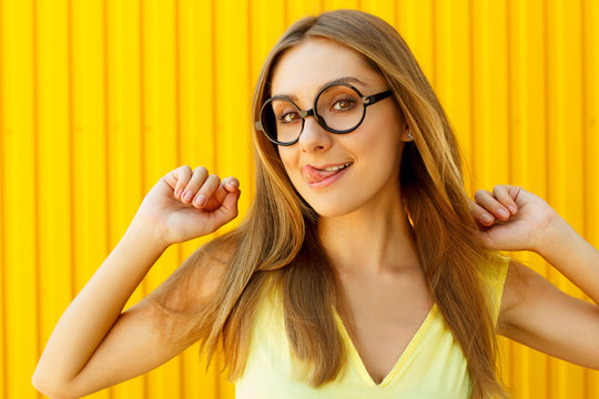 Portrait of a thoughtful girl wearing toy funny glassesshowing her tongue over yellow background at daylight