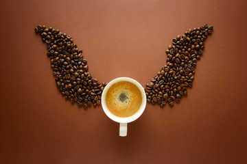 Cup of espresso with wings from coffee beans on brown background. Good morning concept.  Top view....