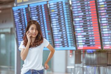 woman in international airport using her mobile phone near the flight information board,