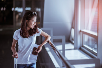 Young woman pulling suitcase in modern airport terminal. Travelling guy with his luggage while waiting for transport. Rear view. Copy space