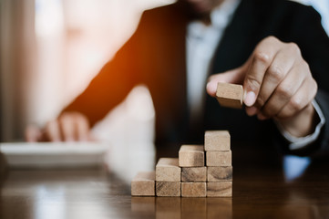 plan and strategy in business.risk concept.hand of man has piling up and stacking a wooden block.Businessman Building The Success.using calculator to calculate.