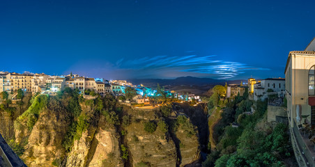 Panorama of Puente Nuevo bridge and the houses built on the edge of the cliff at night with moon light, in the ancient city of Ronda, Spain. © elroce