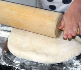 The girl rolls the dough on the kitchen table. We teach children to cook. Learning to cook. Homemade baking.
