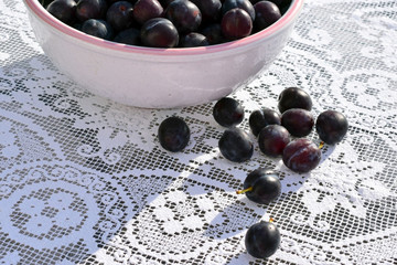 A bowl with ripe plums stands on the table. White vintage tablecloth. Plums lie on the surface of the table. Autumn harvest.