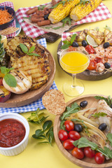 Picnic with grilled food. Sausages and corn on barbecue, shrimp, vegetables and fruits. Delicious summer lunch and plastic dishes. Top view