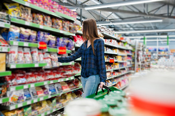 Shopping woman looking at the shelves in the supermarket.  Portrait of a young girl in a market store holding green shop basket.
