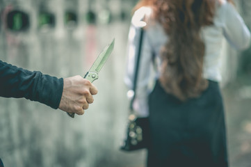 A bandit holds a knife. In order to attack and steal a woman's belongings from the back.