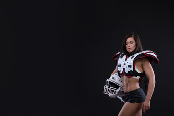 Portrait of sexy attractive young girl in a sports outfit for rugby with the helmet strongly looking forward standing on black background