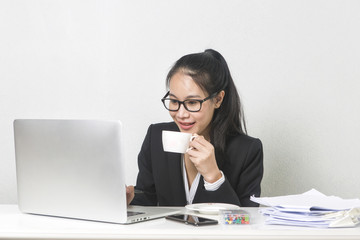Happy business Asian woman working with laptop at white working table, diligent professional working woman drinking coffee while working on laptop computer.