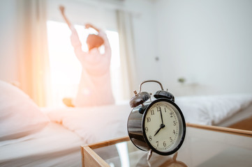 Closeup alarm clock  in bed after waking up, sunlight in morning.