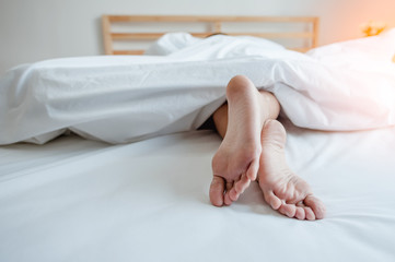 Young female sleeping in bed at home with focus on legs. Feet of woman lying on bed.