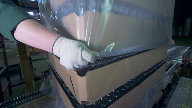 People put wrapping on boxes, close up. Workers wraps boxes with empty bottles at a factory.