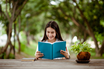 Obraz premium Asian girl reading book at park in summer sunset light. asian woman reading book in Thailand. asian Beautiful woman reading a book at table.