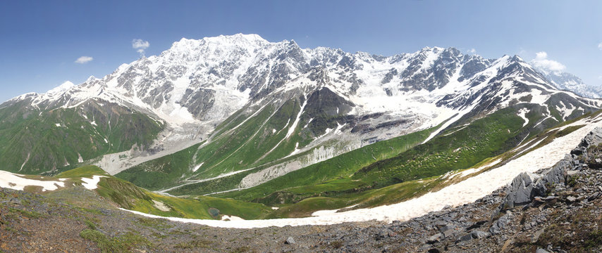 Svaneti mountains landscape in Georgia. Caucasian ridge with snowy mountain peaks and green grass on bright sunny summer day. High mountains in Svaneti. Natural panoramic view on mounts in Georgia