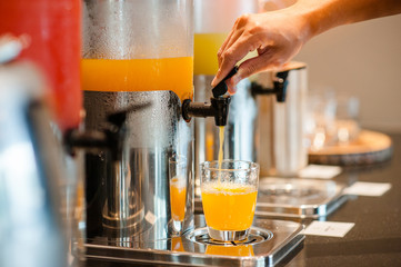 close up hand pulling down the lever of juice dispenser for fresh orange juice.