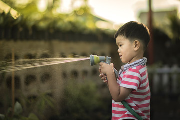 Child is watering to plant in pot at home.