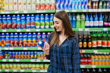 Shopping woman looking at the shelves in the supermarket.  Portrait of a young girl in a market store holding juice.