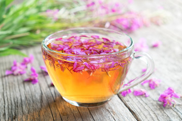 Fireweed healthy tea. Mug of chamerion tea and bunch of medicinal herbs on background, not in focus.