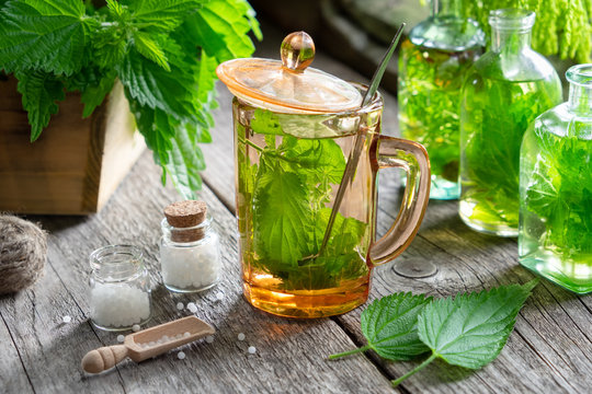 Healthy nettle tea, bottles of infusion, nettle plants and bottle of homeopathic globules on wooden table.