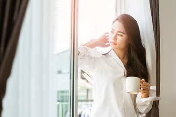 Woman holding a cup of coffee in her hands.Woman drinking coffee at home with sunrise at  window .