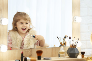 Cute little girl playing with cosmetics in dressing room