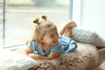 Fototapeta premium Cute little girl lying on window sill at home