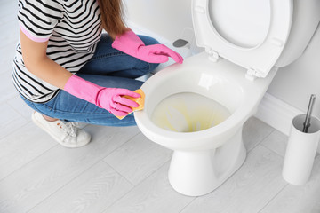 Woman cleaning toilet bowl in bathroom, closeup
