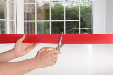 Man cutting red ribbon on blurred background. Festive ceremony
