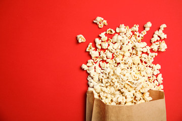 Paper bag with tasty fresh popcorn on color background, top view